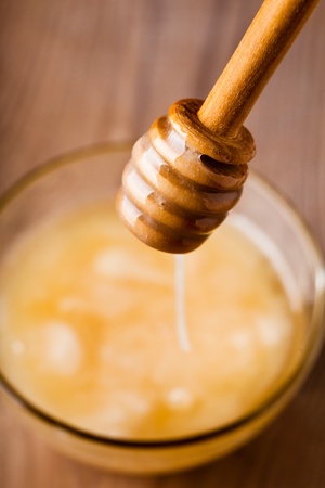 Honey dripping in glass bowl on wooden tableの写真素材
