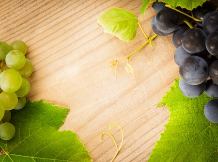 Different grapes with green leaves on wooden tableの写真素材