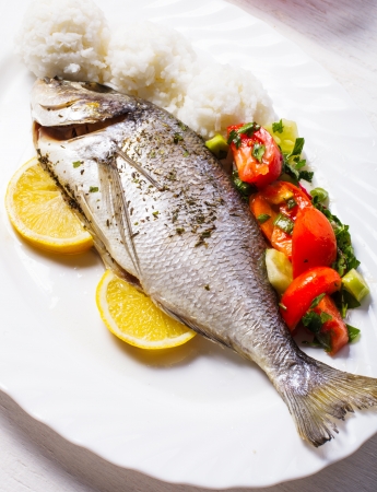 Baked dorado fish with rice and salad on the white plateの写真素材