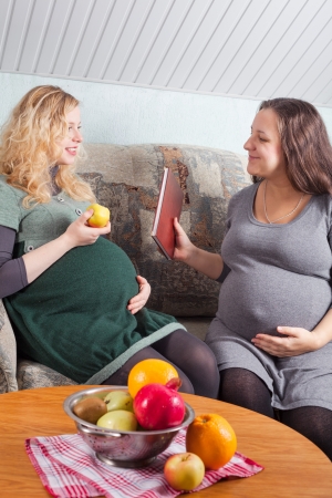 Two pregnant women eat fruits and discuss pregnancy and preparation to parentingの写真素材