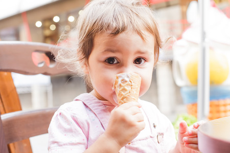 Loverly little girl eats an ice cream in cafe outdoorの写真素材