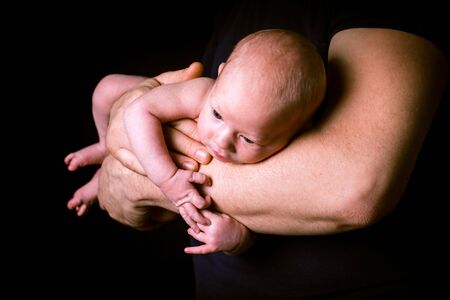 Newborn baby on the father's hands on blackの写真素材