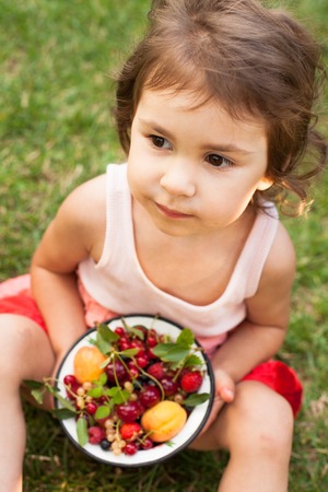 Little girl holds a bowl with summer fruitsの写真素材