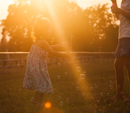Pretty girl runs for the bubbles in the park on the sunsetの写真素材
