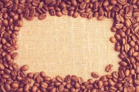Spilled coffee beans frame over burlap textileの写真素材