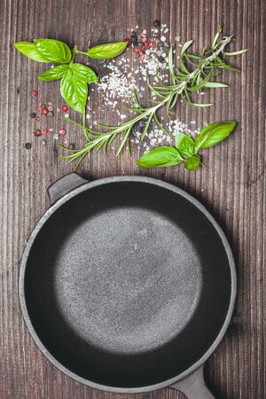 Scattered fresh basil and rosemary, sea salt and dry peppercorns near the frying panの写真素材