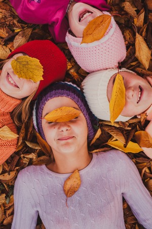 Four girls playing with autumn leaves, lying with closed eyesの写真素材