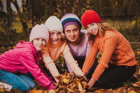 Four girls playing with autumn leaves and smiling