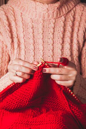 The hands that hold needles and knitting a red warm jacket