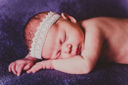 Sleeping baby with a white lace on his head lying on stomach on purple blanketの写真素材