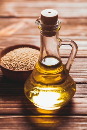 Sesame oil in a glass bottle with a cork and heap sesame seeds in a wooden bowlの写真素材