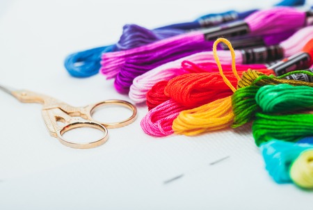 Close up of embroidery needle, colour floss and scissors on canvas