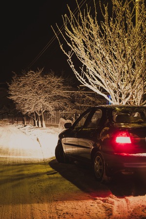 Bright headlights of a black car illuminate the snow-covered road in winterの写真素材