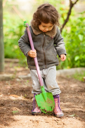 Little girl in rubber boots holding a shovel and tried to digの写真素材