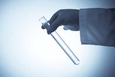 Hand in rubber glove holding a test tube with transparent liquid on blue backgroundの写真素材