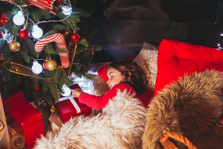 The little dark-haired girl lying on the floor near the gifts  and Christmas treeの写真素材