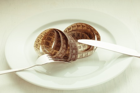 Fork and knife with meter on the empty white plate, diet concept