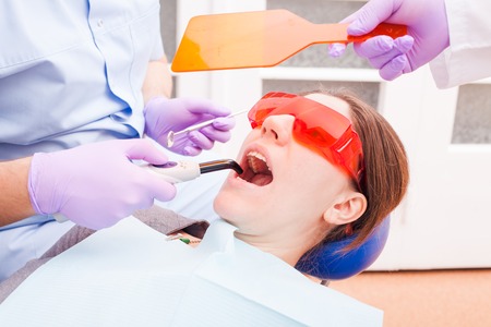 The patient lies in special glasses for protection against laser beams while the dentist works with dental curing lightの写真素材