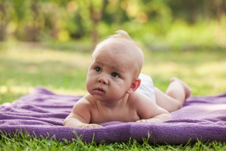 Naked little boy wearing a diaper learning to crawl on green grassの写真素材
