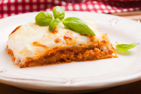 Piece of lasagna bolognese with basil leaves in a white plateの写真素材
