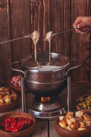 Delicious Cheese Fondue on a fork on a wooden standの写真素材