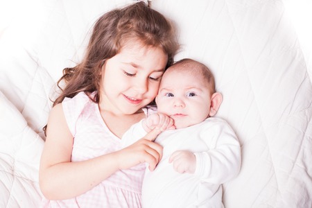 Pretty little girl laying with her adorable brother on the soft backgroundの写真素材