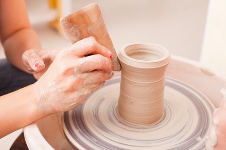Hands of girl who tries to make pottery from white clay on a potter's wheelの写真素材