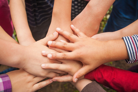 Close-up of many children's hands holding together as a team on a nature background