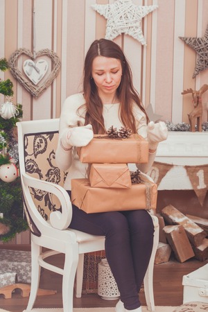 Girl in gloves holding  gift boxes on her knees near Christmas treeの写真素材