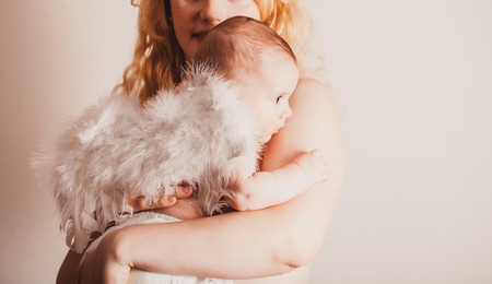 Pretty mom embracing her beautiful baby with wings of an angel isolated on whiteの写真素材