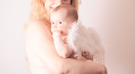 Pretty mom embracing her beautiful baby with wings of an angel isolated on whiteの写真素材