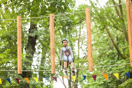 A boy in a helmet and safety equipment in adventure ropes park on the background of nature