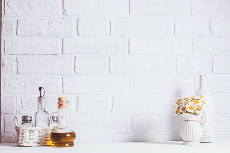 Home interior decoration, bouquet of daisies in white vase, decorative white bottle and glass bottle of oil in a basketの写真素材