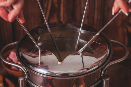 Delicious Cheese Fondue on a fork on a wooden standの写真素材