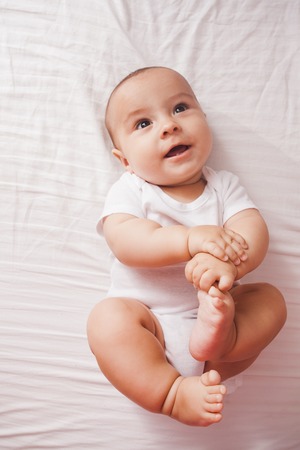 Top view of a cute baby lying on a bed with raised feet up