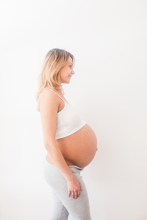 Pregnant woman is standing near white wallの写真素材