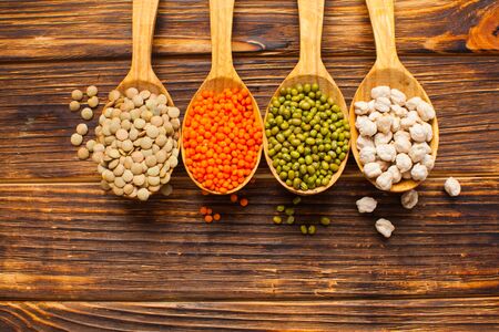 Flat lay composition with spoons full of different types of beans on wooden background.