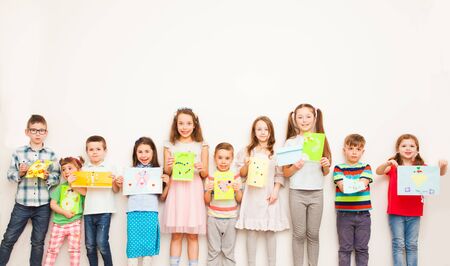 Happy kids showing their greeting card over white wall. Handmade paper crafts for kidsの写真素材