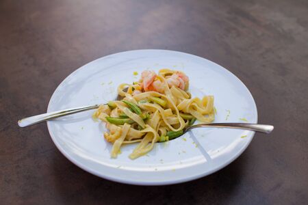 Close up of a plate of pasta topped with shrimps and baby beans