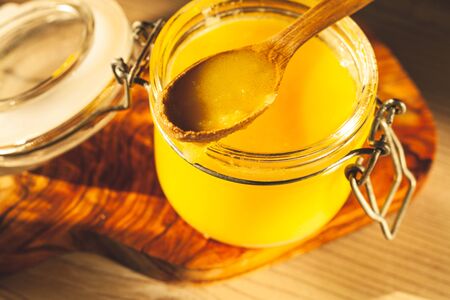 Wooden spoon with ghee - clarified butter in the glass jar at the kitchen, sunny day