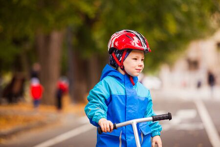 Cute preschooler boy in safety helmet riding a scooter.の写真素材