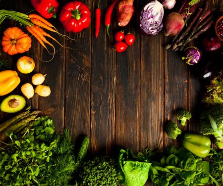 Circle of fresh vegetables, greens and herbs on dark wooden background. Multicolor organic...