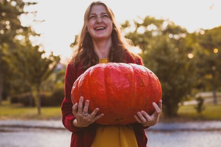Woman with giant pumpkin in the hands, celebrating happy Thanksgiving dayの写真素材