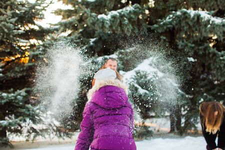 Joyful daughter throwing snowball at parents in winter park. Happy winter holidaysの写真素材