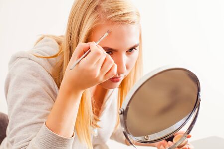 Blonde woman applying dry cosmetic tonal foundation on the face using makeup brushの写真素材
