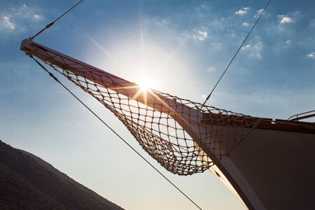 Wooden bowsprit of yacht with a hanging net on the background of sunset