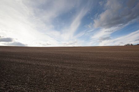 Plowed field prepared for planting crops at sunset. Farm land and blue cloudy sky