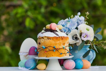 Easter holiday concept. Orthodox sweet bread - kulich, with icing and macarons on top, flowers in...