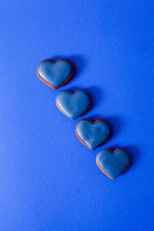 Four tasty gingerbread cookies with blue sugar icing on top, in diagonal row on trendy blue background. Minimalistic concept for Valentines day greetings. Top view, flat lay, copy spaceの写真素材