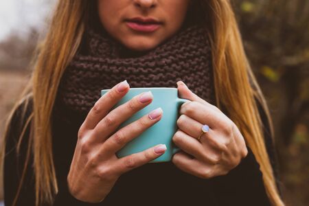 Female hands with tender pink nail design holding blue cup outdoors. Woman beauty and wellness. Girls hand with modern ring.の写真素材